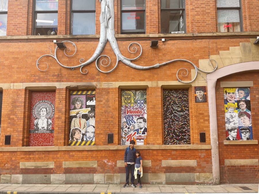 Two kids stand outside Afflecks Palace, a red brick building daubed in images of famous Manchunians