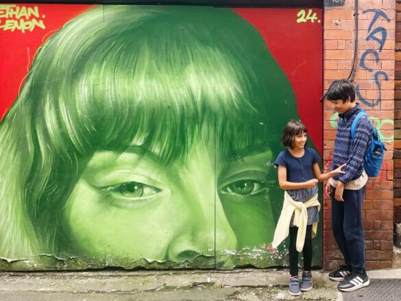 2 kids stand in front a bold mural of a green woman